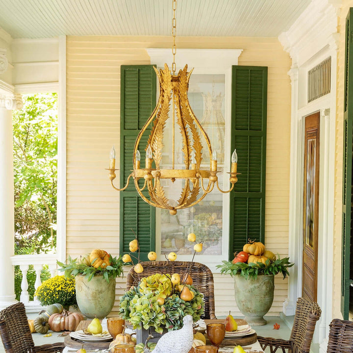 Decorative outdoor setting with a gold chandelier, green shutters, and autumn-themed table setting.