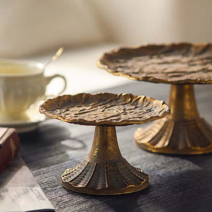 Two decorative antique gold stands on a wooden surface with a blurred background