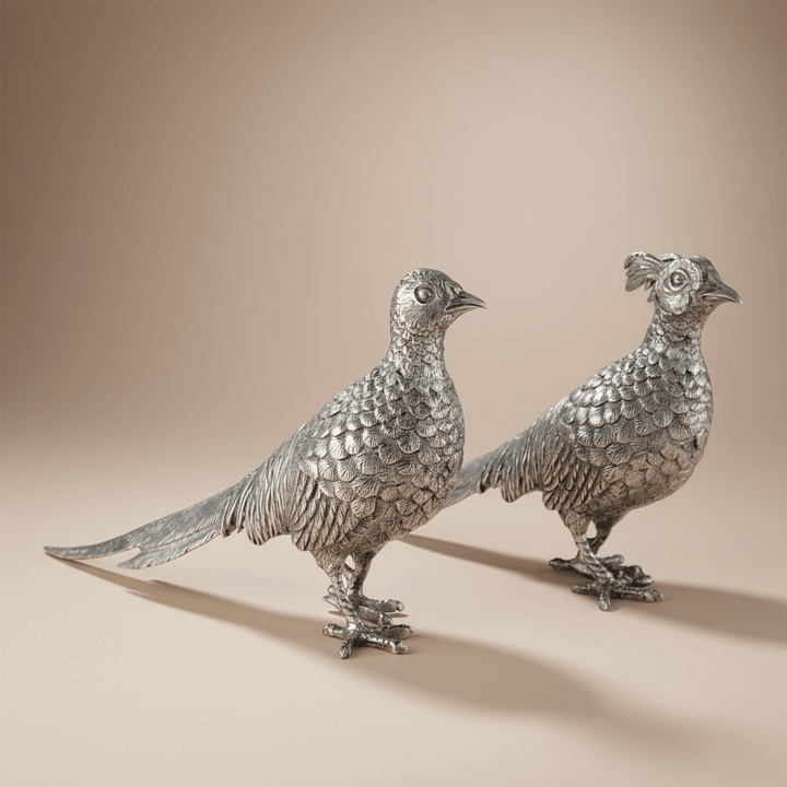 Two silver pheasant sculptures on a beige background