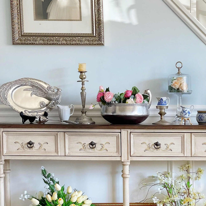 Decorative table with flowers, candles, and a framed picture on a light blue wall.
