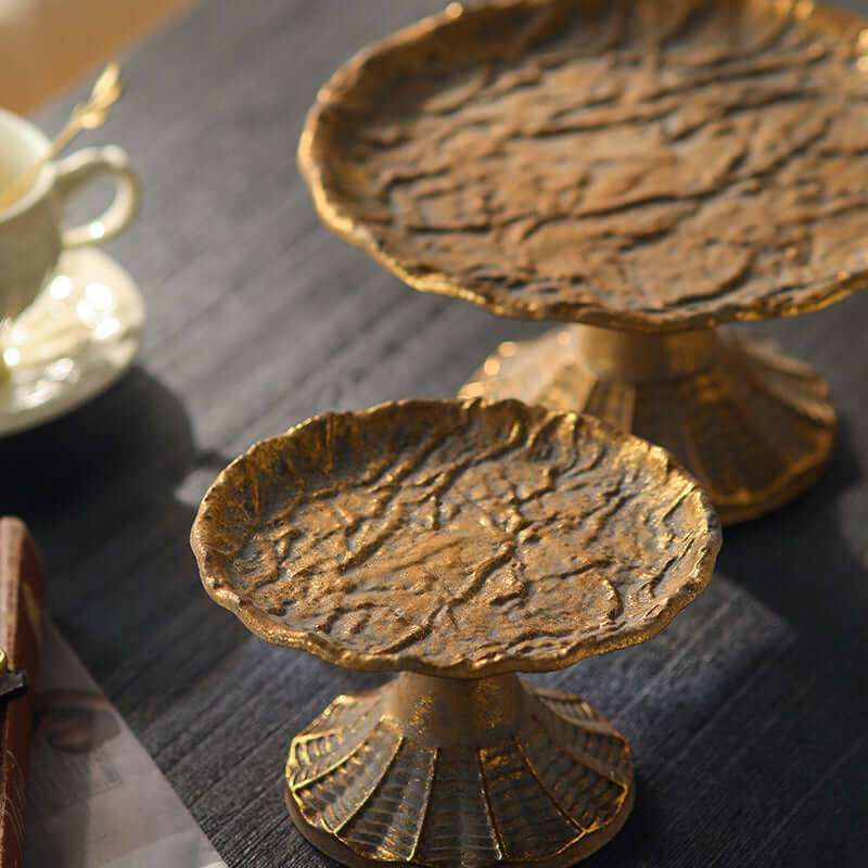 Two gold display stands s on a dark surface with a blurred cup in the background.