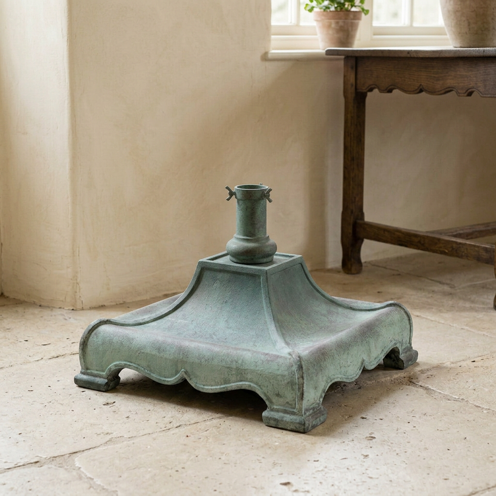 Hearthmere Christmas tree stand in Verdigris on a pale stone floor, showing its scalloped base and central tree holder.
