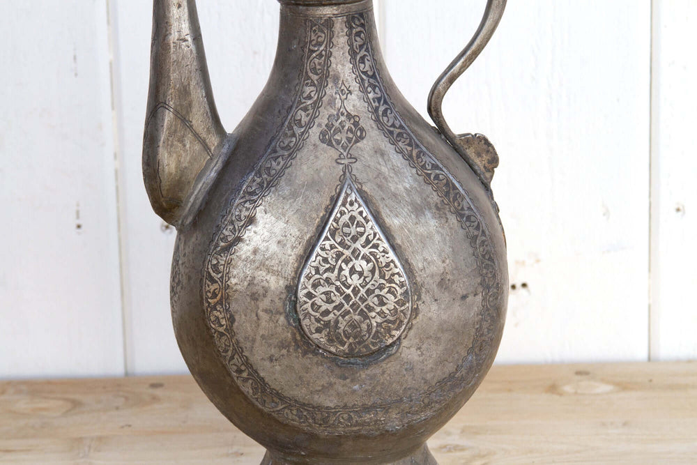 Decorative metal pitcher with intricate patterns on a wooden surface.
