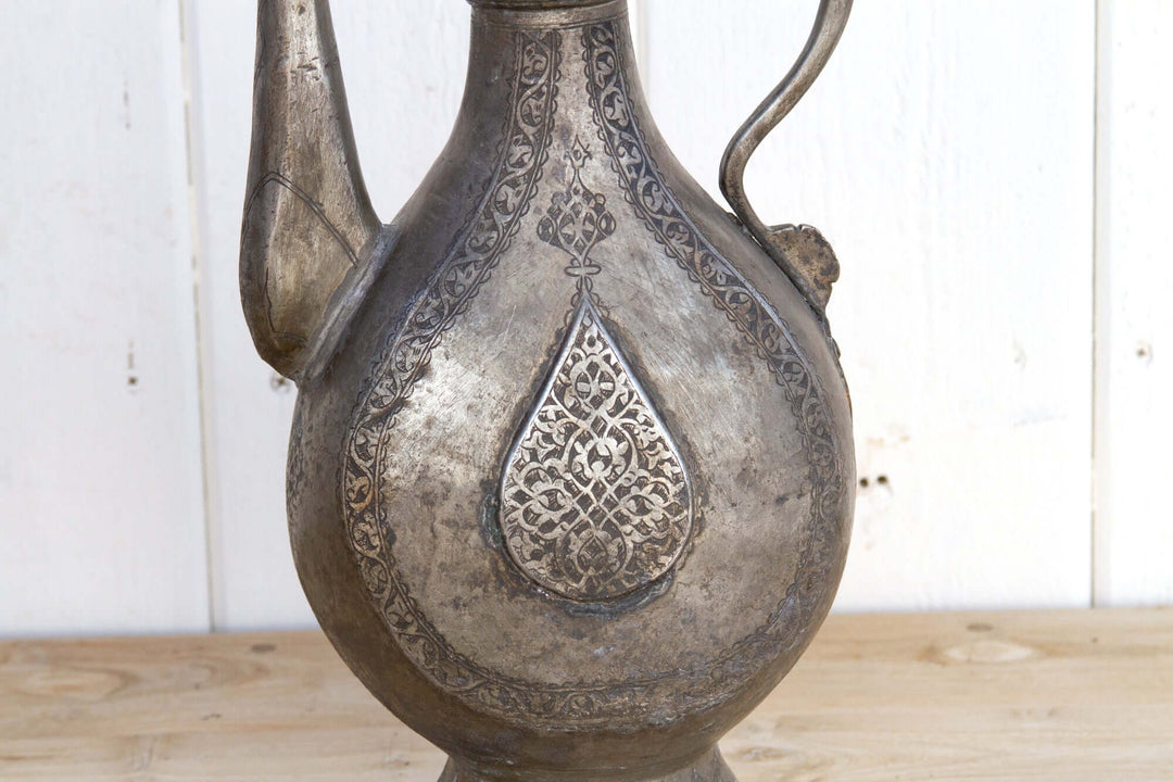 Decorative metal pitcher with intricate patterns on a wooden surface.