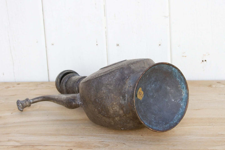Vintage-style metal oil lamp on a wooden surface with a white paneled background