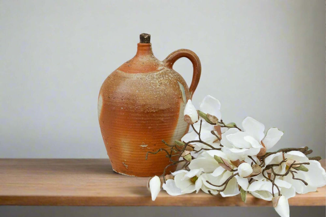 Ceramic pitcher on a wooden surface with white flowers against a plain background