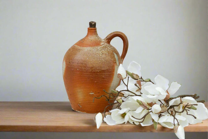 Ceramic pitcher on a wooden surface with white flowers against a plain background