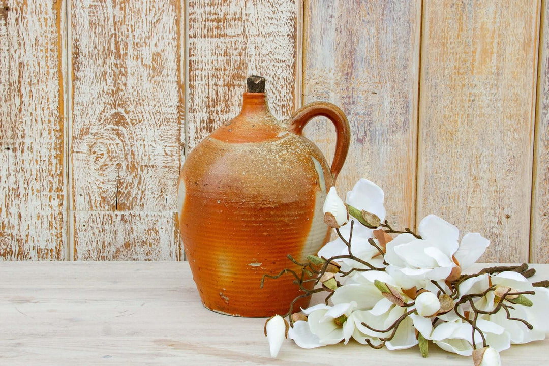 Brown ceramic jug with white flowers on a wooden surface