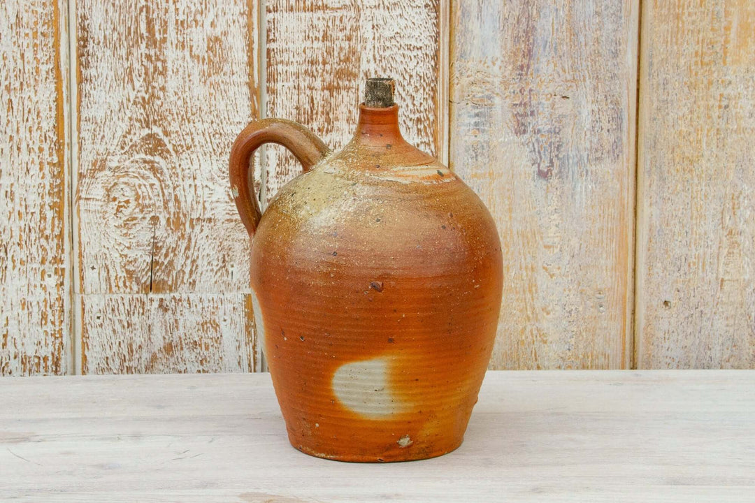 Vintage ceramic jug with a rustic brown finish on a wooden surface.