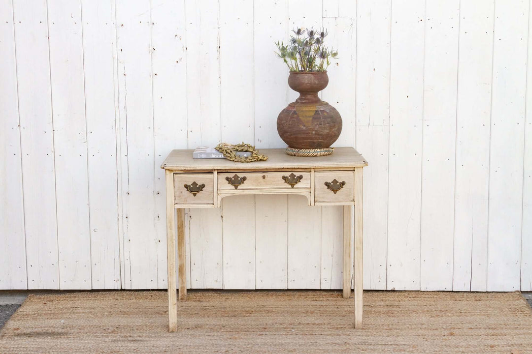 Wooden console table with decorative elements against a white paneled wall.