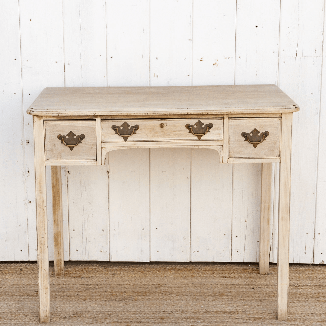 Light wooden desk with three drawers against a white paneled wall.