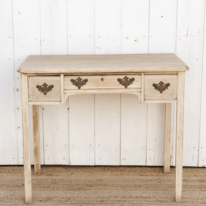 Light wooden desk with three drawers against a white paneled wall.