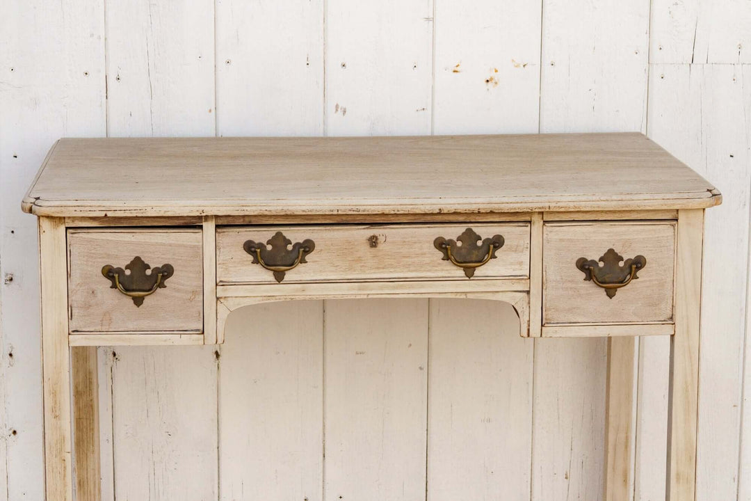 Vintage wooden desk with metal handles against a white paneled wall