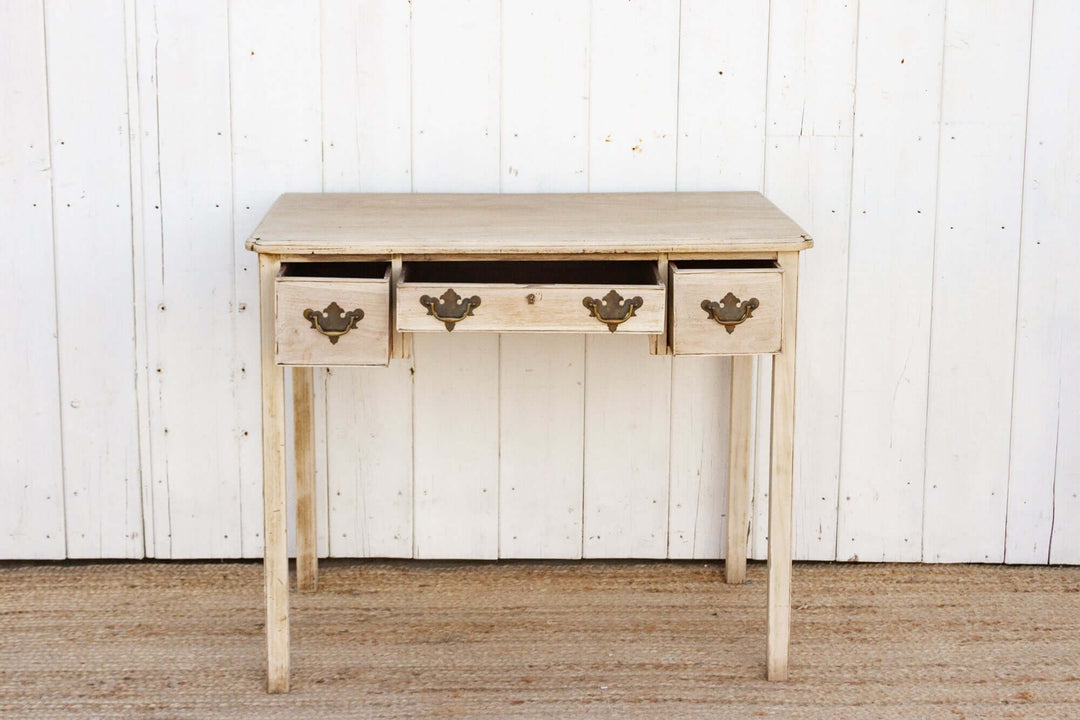 Wooden console table with three drawers against a white paneled wall.