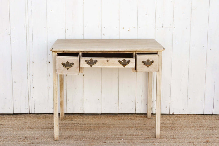 Wooden console table with three drawers against a white paneled wall.