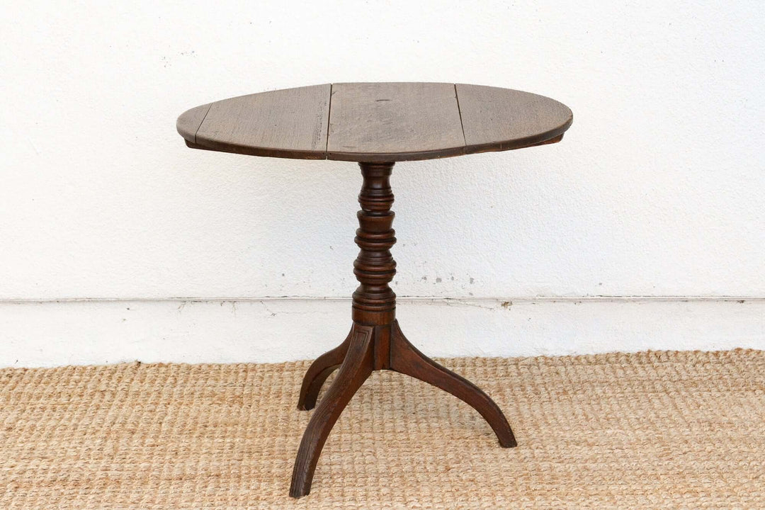 Round wooden table with a pedestal base on a white wall background