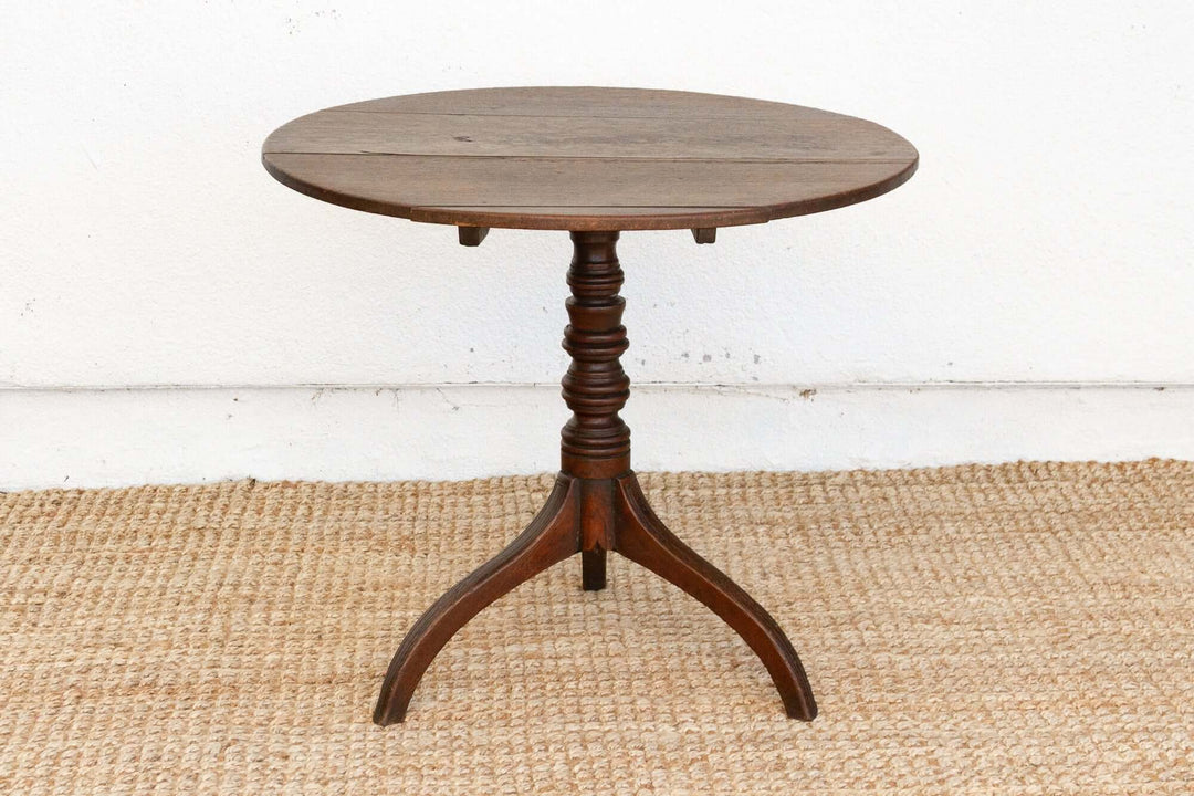 Wooden round table with a pedestal base on a woven mat against a white wall