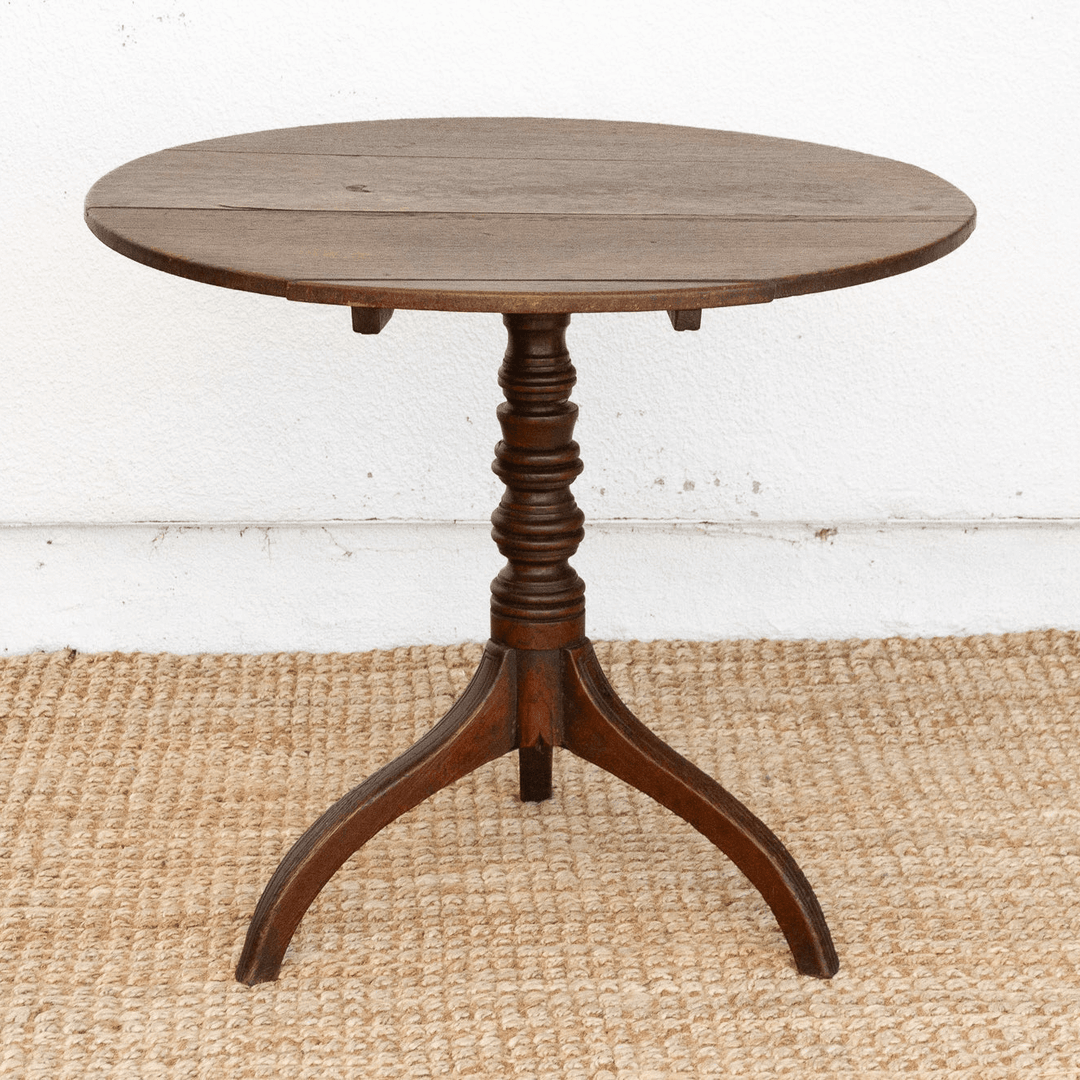 Round wooden table with a pedestal base on a textured floor.