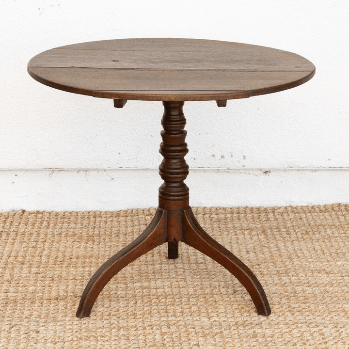 Round wooden table with a pedestal base on a textured floor.
