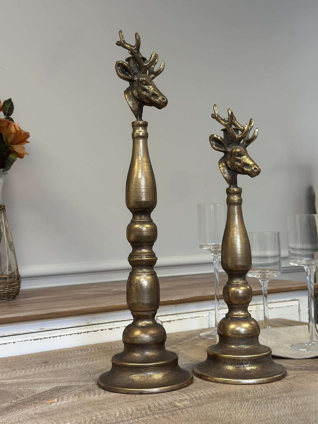 Vintage Brass Deer Head Candle Holders with sculpted antlers on turned bases, set against a wooden and glass backdrop.