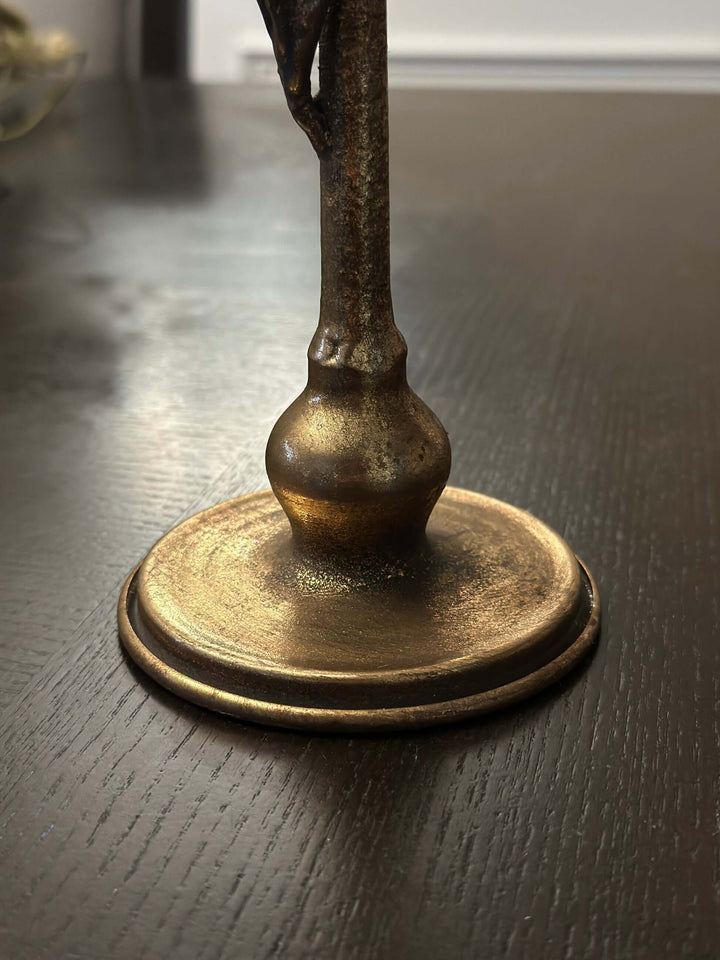 Close-up of an antique brass candle holder base with a leaf design, highlighting its vintage golden-bronze patina.