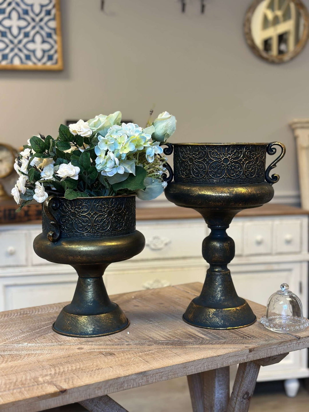 Antique bronze ornate metal urns with floral decoration, showcasing old-world European style on a wooden table in a classic setting.