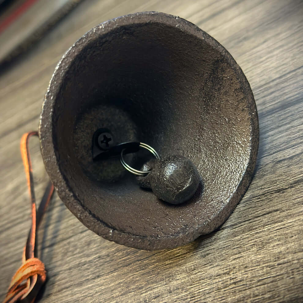 Black metal bell with a leather strap on a wooden surface