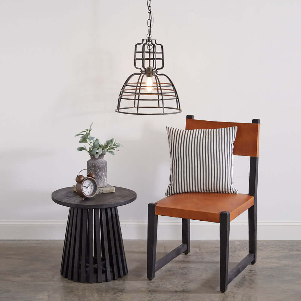 Industrial cage pendant light hanging above a stylish chair and table, enhancing modern decor with rustic charm.