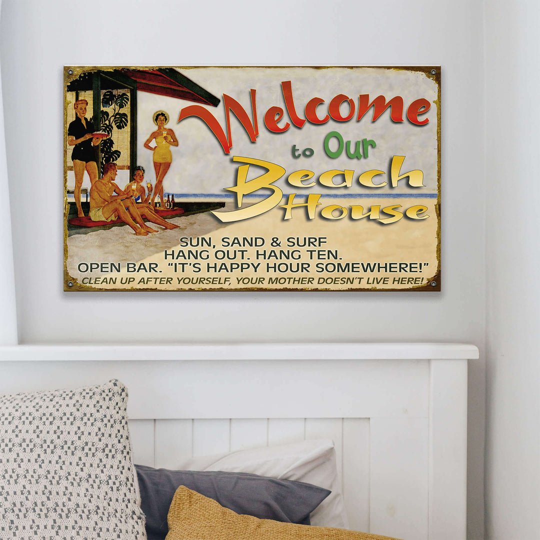 Vintage-style 'Welcome to Our Beach House' sign on a wall above a bed.