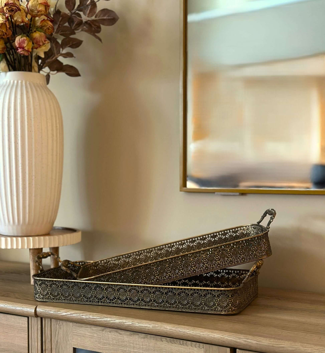 Antique Brass Filigree Serving Tray Set displayed on a wooden sideboard next to a decorative vase.
