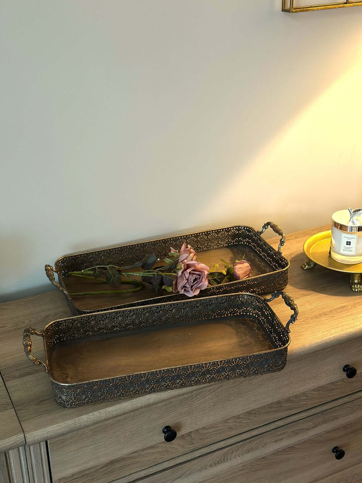Antique brass filigree serving tray set on wooden surface with pink roses, showcasing intricate vintage design and warm patina.