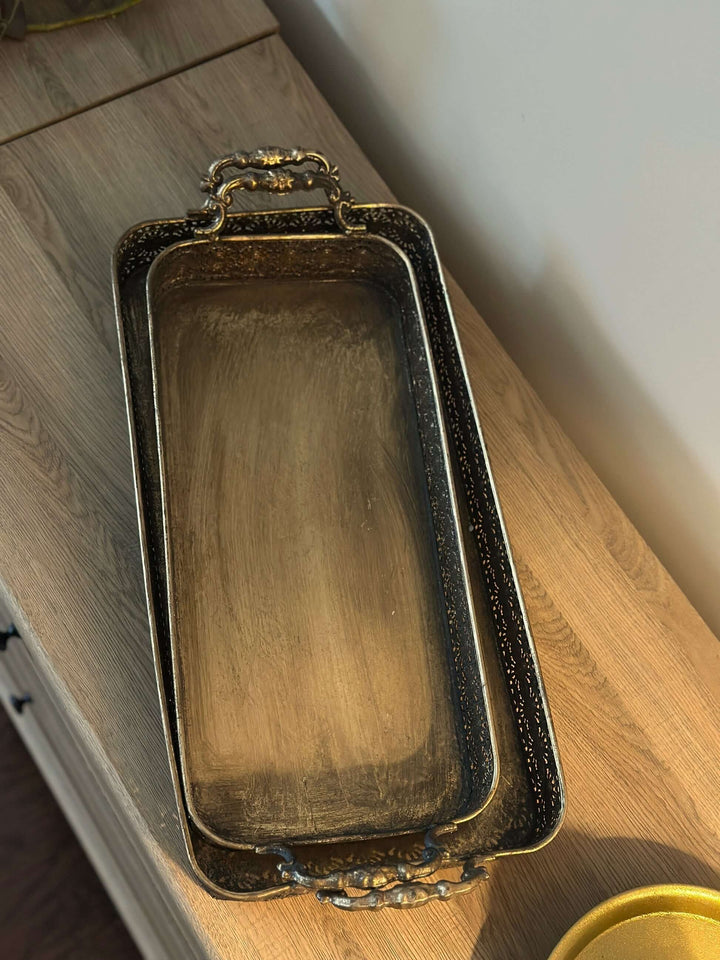 Antique brass filigree serving trays with handles on a wooden surface, showcasing intricate metal craftsmanship and vintage elegance.
