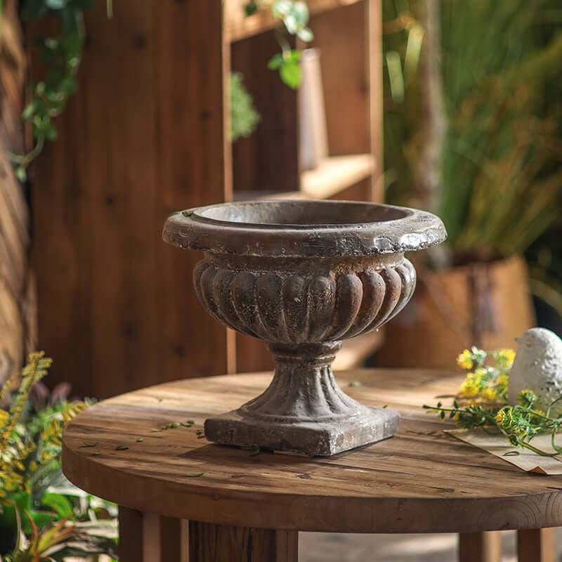 Decorative stone urn on a wooden table with a garden setting