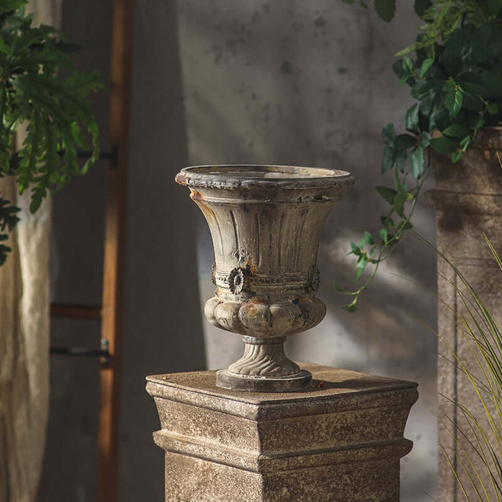 Decorative stone urn on a pedestal with plants in the background