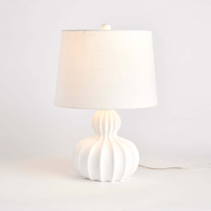 White carved wood table lamp with curved base and fluted design, featuring a linen shade for soft lighting.
