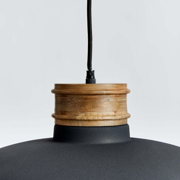 Close-up of industrial pendant light featuring matte black shade and turned wood neck in matte charcoal finish.