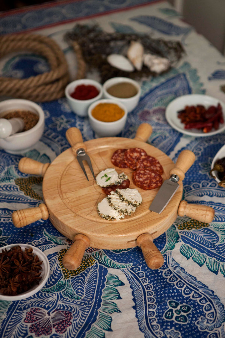 Wooden cheese board with various spreads on a patterned tablecloth