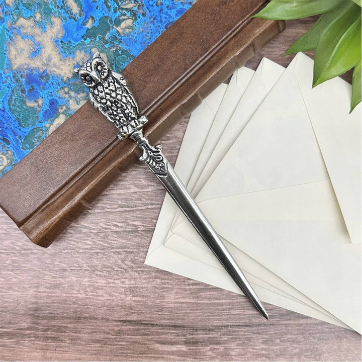 Decorative letter opener with owl design on a wooden block next to white envelopes.
