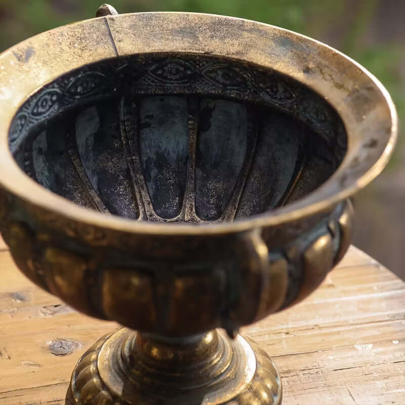 Decorative bronze urn on a wooden surface with a blurred natural background