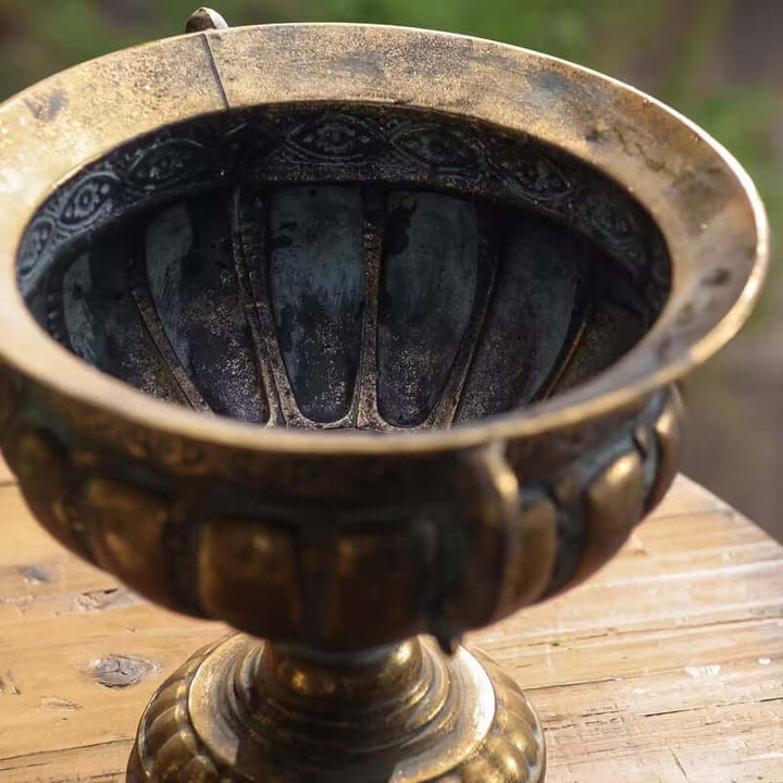 Decorative bronze urn on a wooden surface with a blurred natural background
