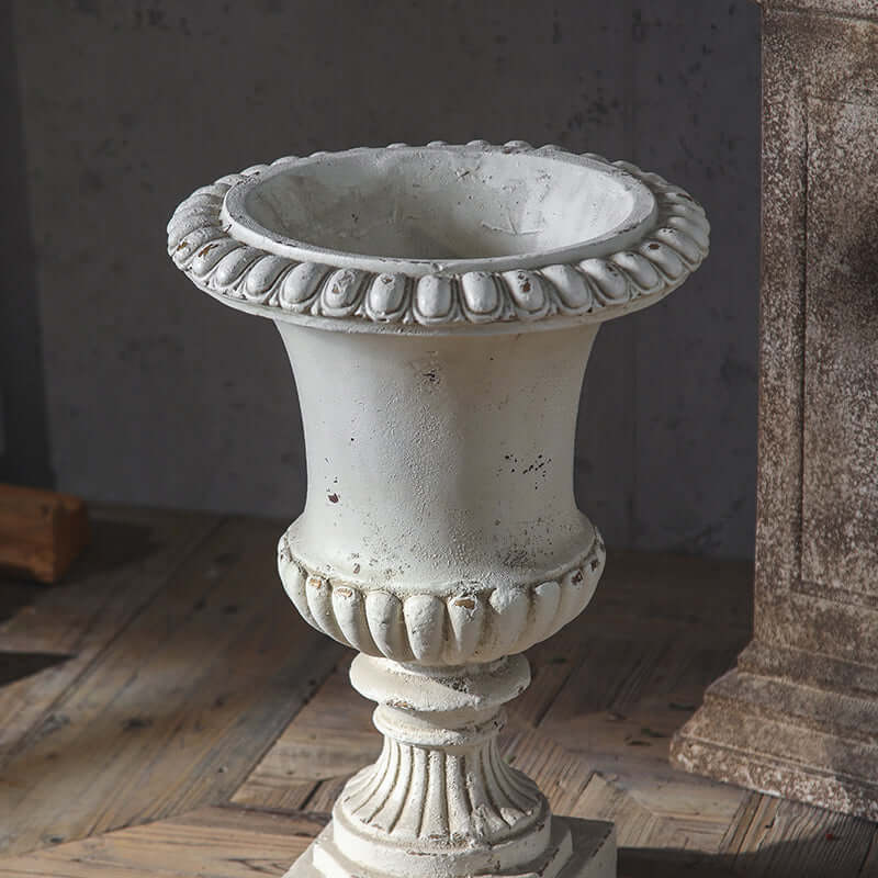 Decorative stone urn on a wooden floor with a textured wall in the background