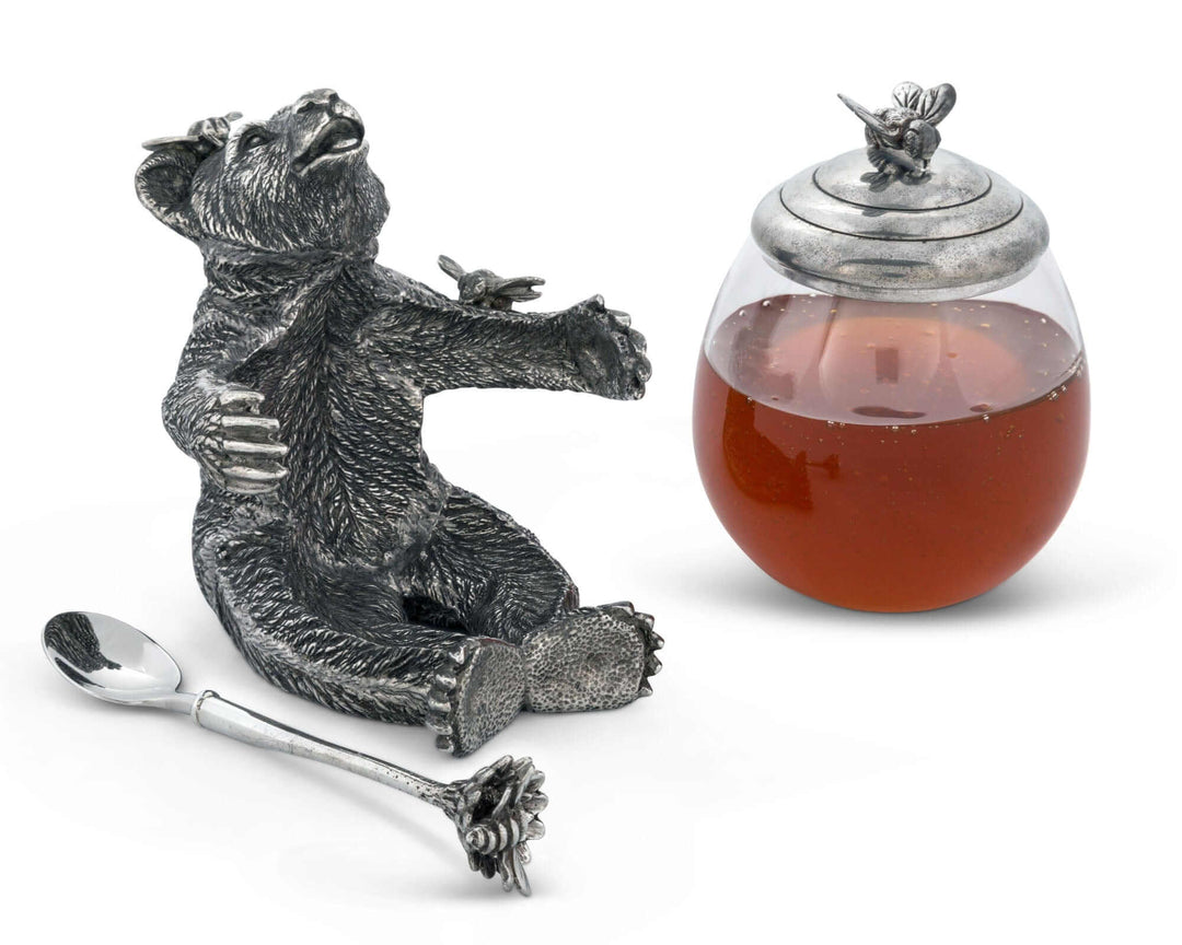 Decorative honey jar with bear sculpture, spoon, and honey inside on a white background