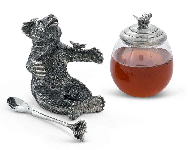 Decorative honey jar with bear sculpture, spoon, and honey inside on a white background