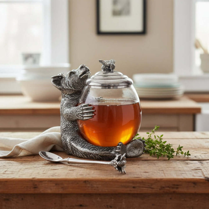 Decorative honey jar with a bear design and a spoon on a white background