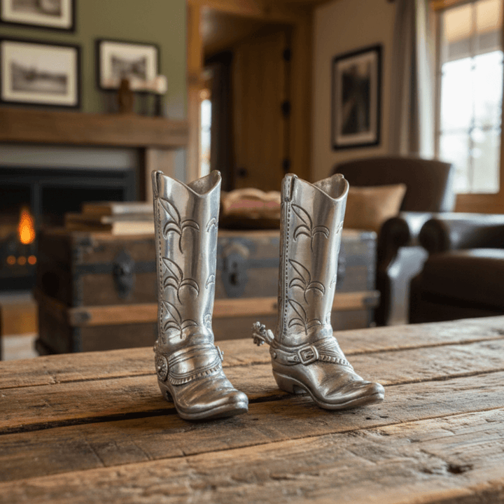 Silver cowboy boots salt and pepper shakers on a wooden table in a cozy living room with a fireplace.