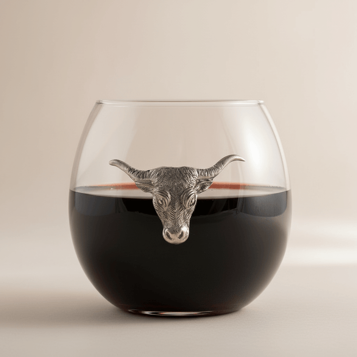 Glass with bull head decoration filled with red wine on a beige background