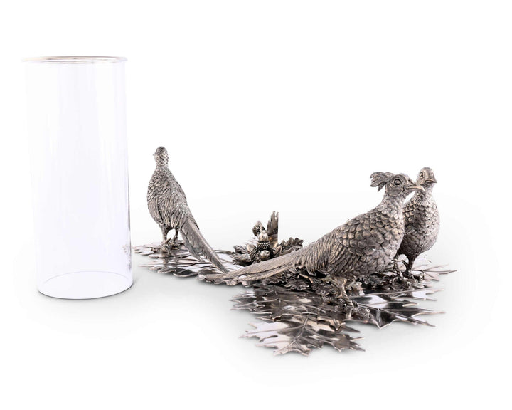 Decorative metal sculpture of three birds on a branch with a clear glass candle hurricane beside it.