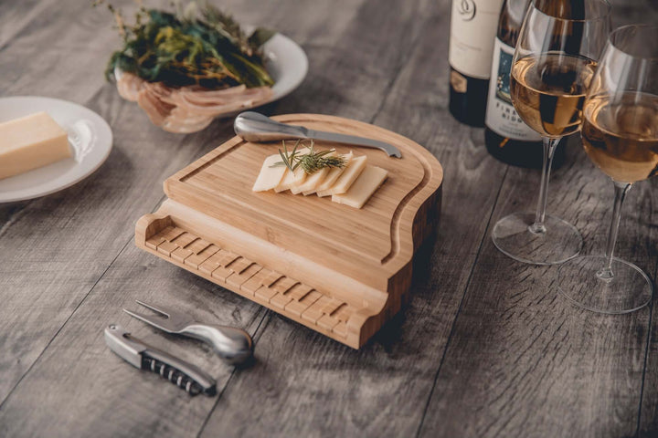 Wooden cheese board with sliced cheese on a wooden table with wine glasses and bread.