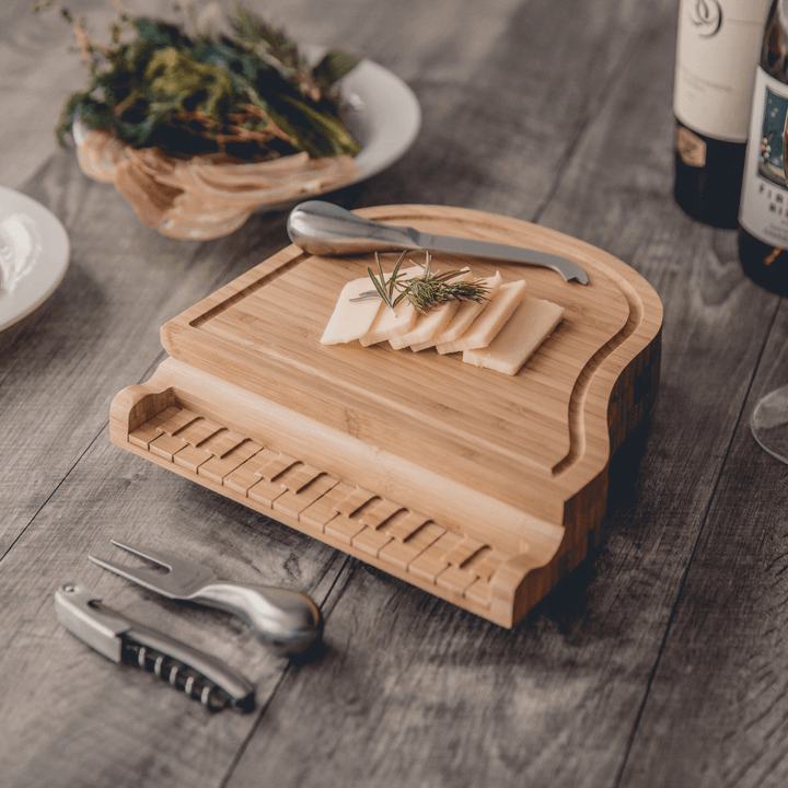 Piano Cheese Board and Knife Set on table with sliced cheese and utensils, showcasing bamboo craftsmanship inspired by a grand piano design.