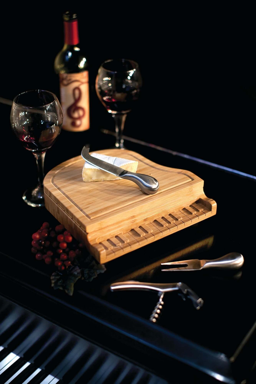 Wooden cheese board with a bottle of wine, glasses, and cheese on a dark surface.